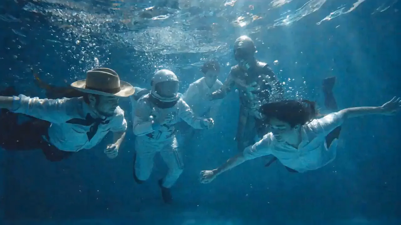 Swimmers in hats and diving helmets joining hands underwater.