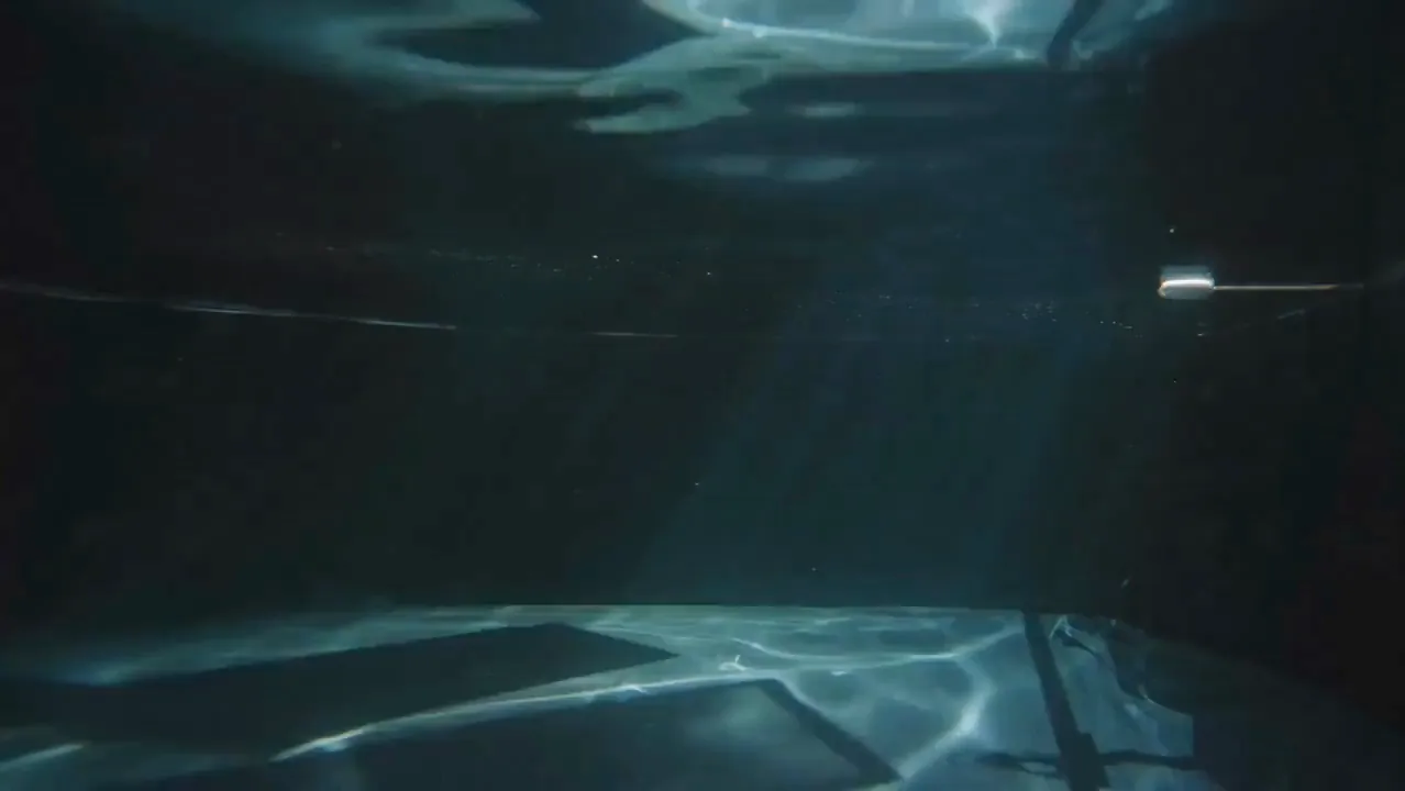 An underwater room holding a vintage television, a flight case and a film reel in a glass box.
