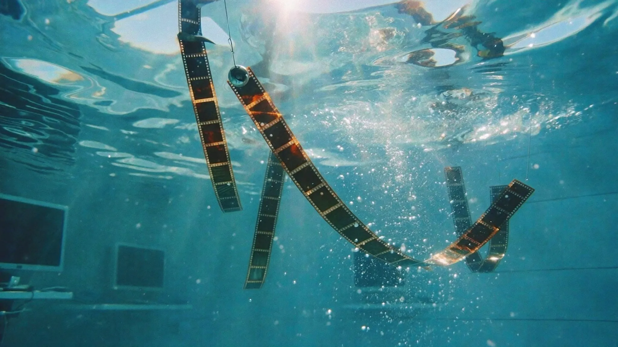 Strips of exposed film hanging in the water, lit from the surface.